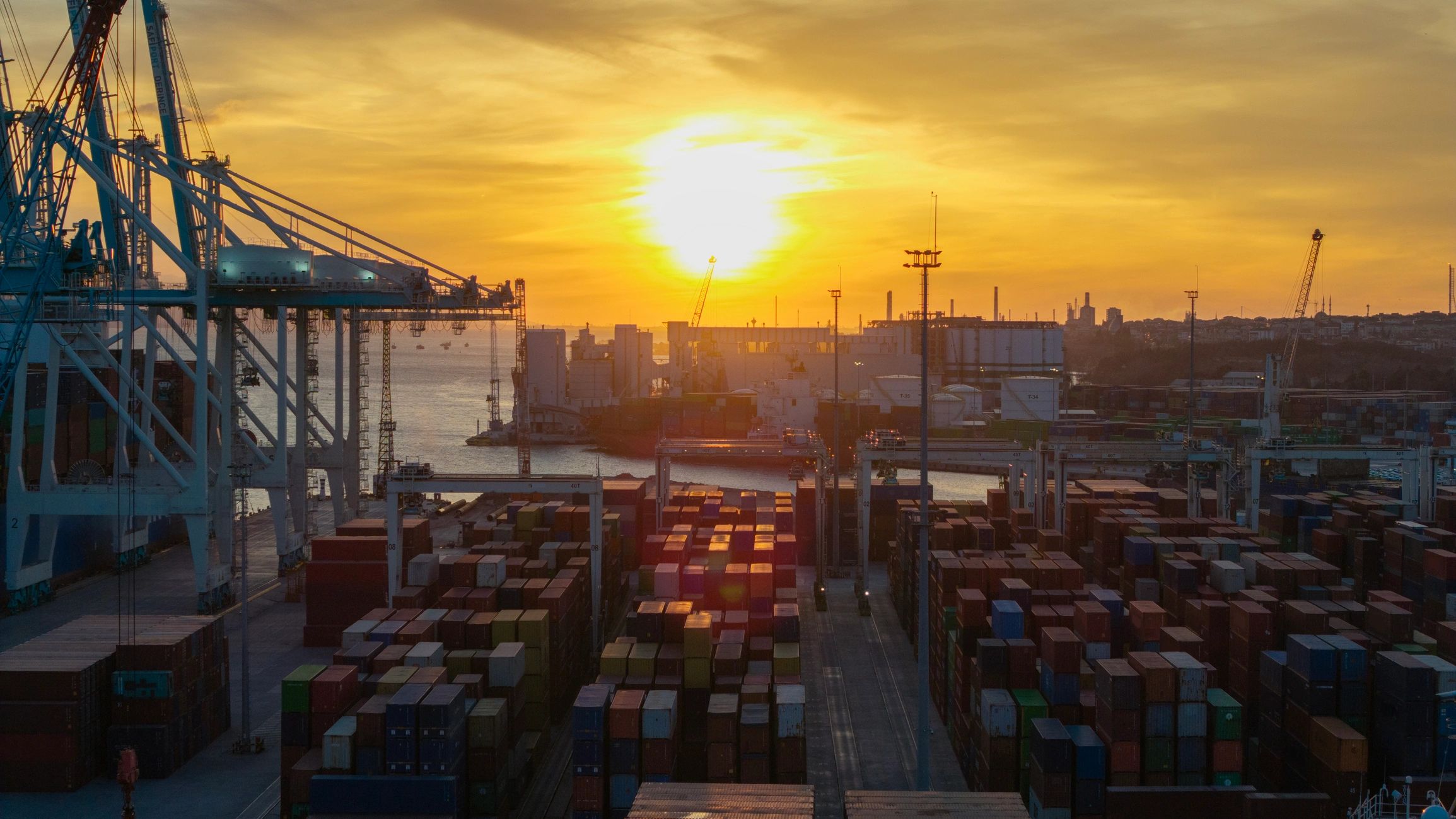 Aerial view of a container port with stacked cargo and cranes at sunset